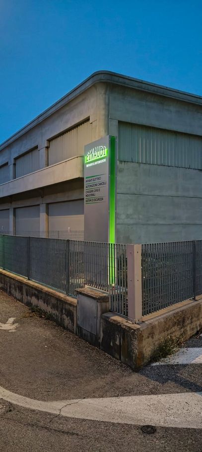 Angolo di un edificio grigio al crepuscolo, con un'insegna illuminata di verde e un marciapiede recintato.