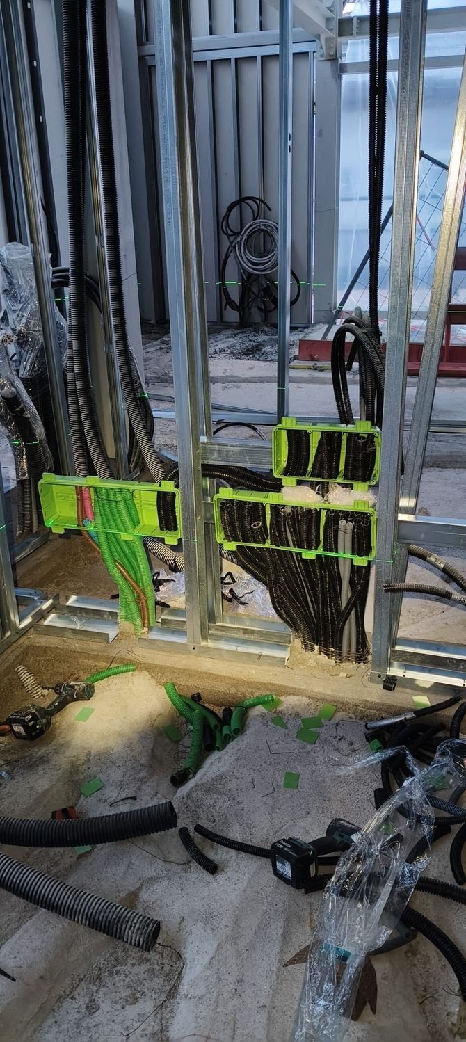 Cantiere edile con ringhiere di sicurezza verdi e una scala tra barre d'armatura a vista e detriti di cemento.