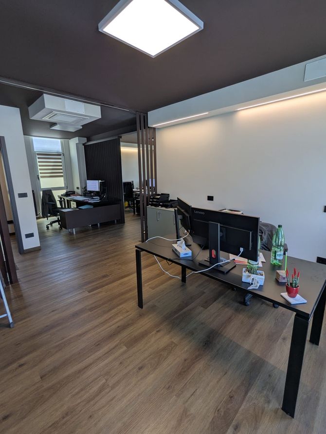 Ufficio moderno con pavimento in legno, pareti bianche, scrivanie, monitor e un'area salotto sul retro.