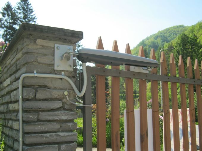 Pilastro in pietra con scatola di derivazione e canalina elettrica accanto a una recinzione in legno in un cortile esterno soleggiato.
