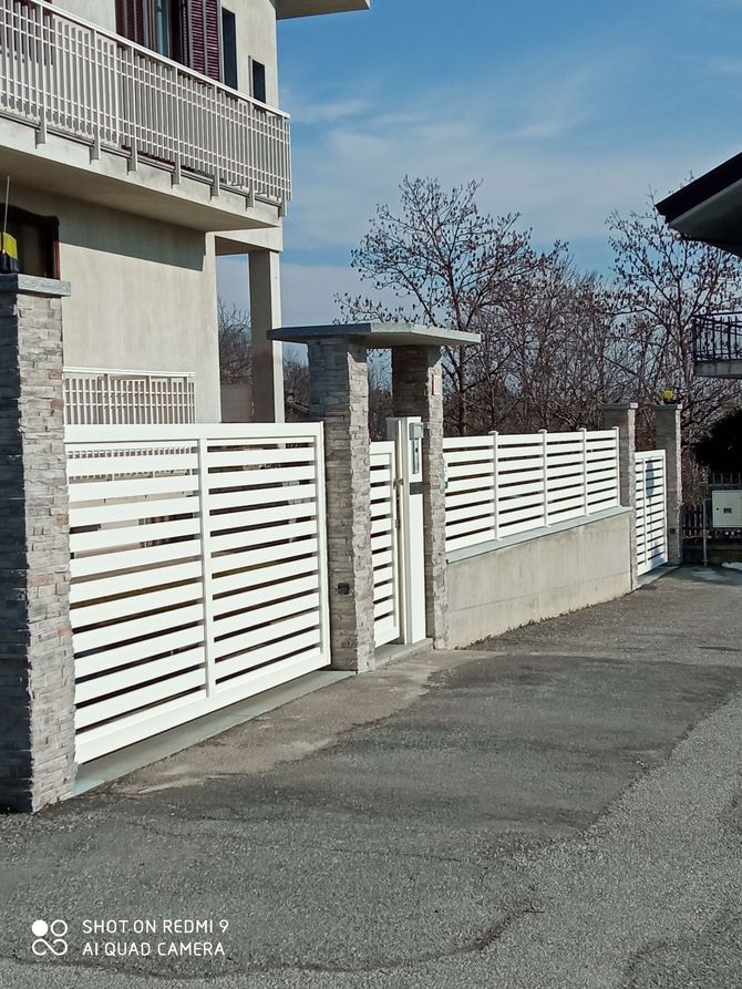 Via residenziale con una recinzione a doghe bianche accanto a un palazzo di appartamenti beige sotto un cielo limpido