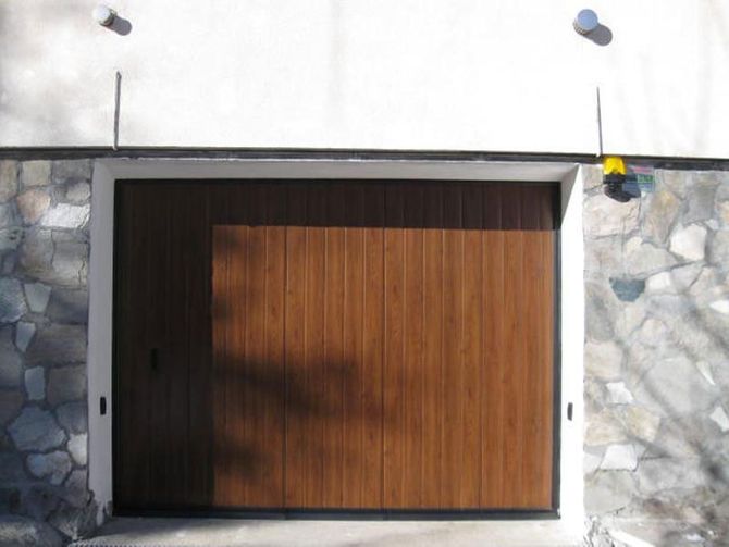 Porta da garage in legno incastonata in un muro di pietra con telaio bianco e parte superiore bianca.