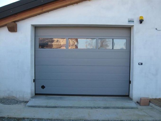 Porta del garage grigia chiusa su una casa in stucco bianco con piccole finestre vicino alla parte superiore