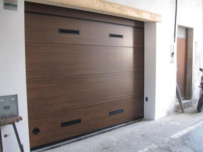 Ampio portone da garage marrone con strette finestre nere, incastonato in una facciata bianca dell'edificio.