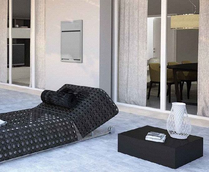 Patio moderno con chaise longue nera, tavolino basso e porte scorrevoli in vetro sullo sfondo.