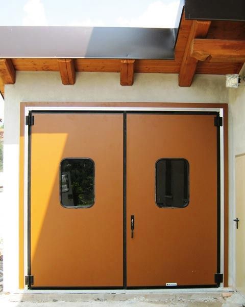 Doppie porte arancioni con piccole finestre sotto una tettoia in legno all'ingresso di un edificio