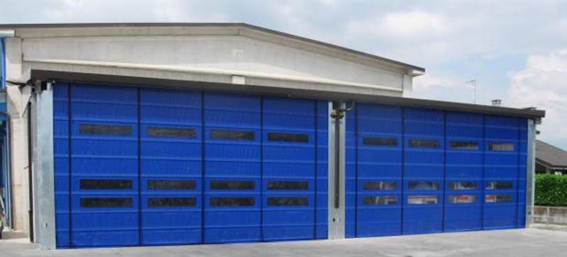 Garage industriale blu con numerose porte avvolgibili chiuse su un edificio bianco.