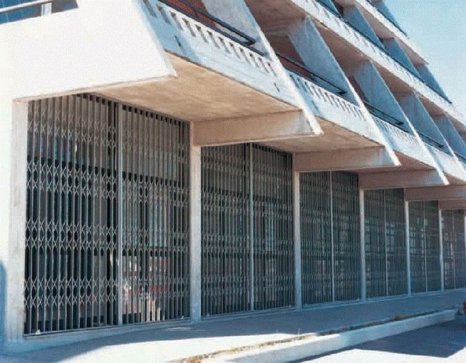 Facciata moderna dell'edificio con cancelli di sicurezza in metallo e aggetti inclinati in cemento.