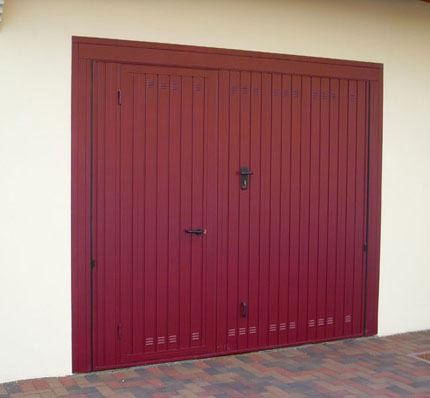 Porta da garage rossa con pannelli verticali incastonata in una parete beige accanto a un vialetto piastrellato.