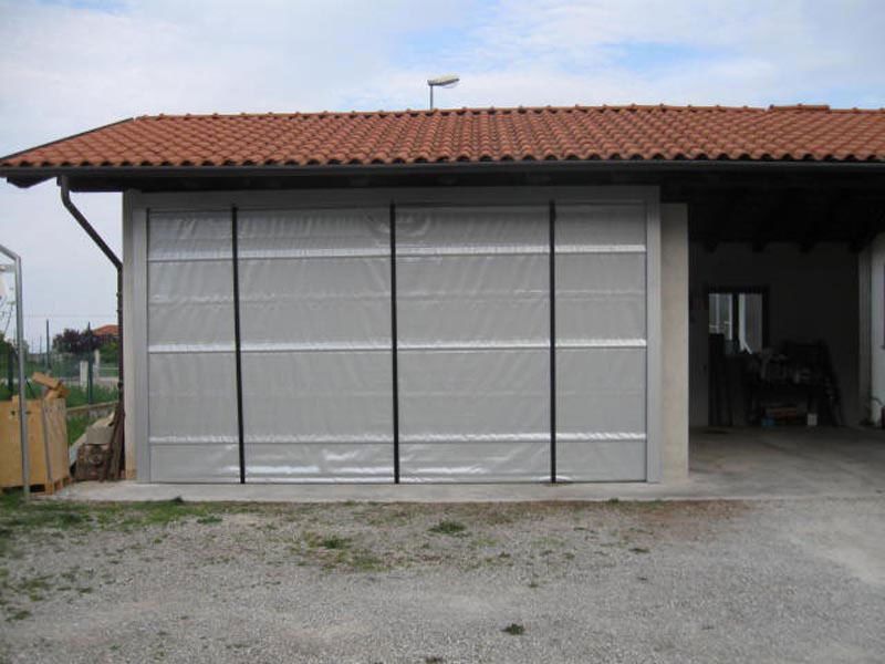 Porta avvolgibile grigia su un piccolo edificio con tetto di tegole rosse e vialetto di accesso in ghiaia.