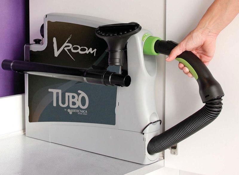 Mano che impugna un manico verde e nero attaccato a un aspirapolvere Vroom Tubo montato a parete.