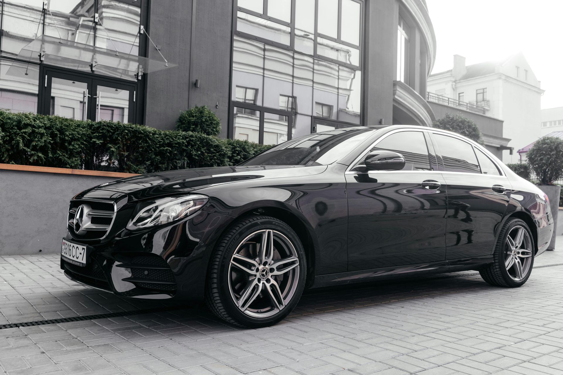 Black luxury sedan parked outside a modern building on a cobblestone street