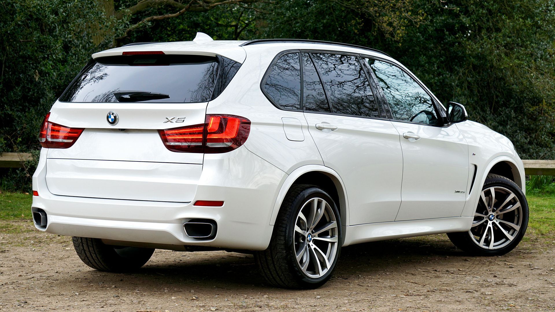 White BMW SUV parked on gravel, rear three-quarter view