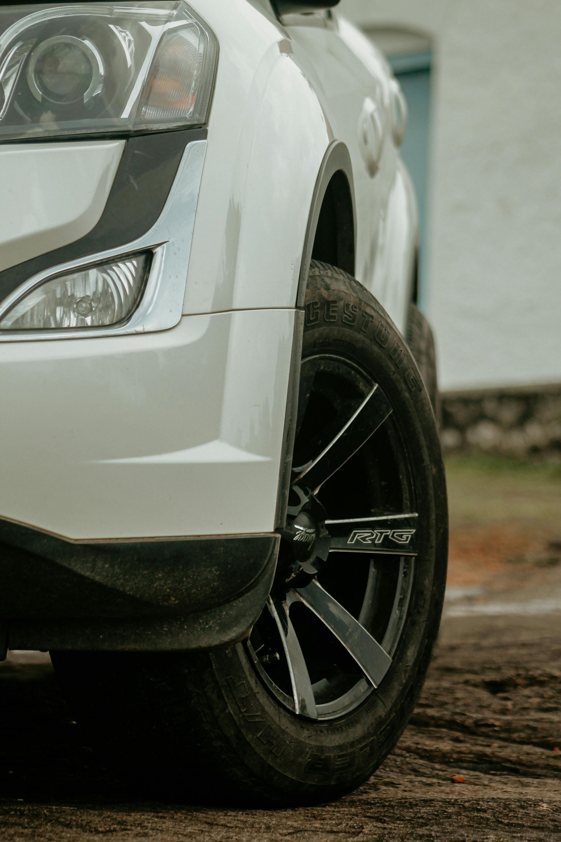 Front-left view of a white SUV with black alloy wheel parked on a wet, muddy road