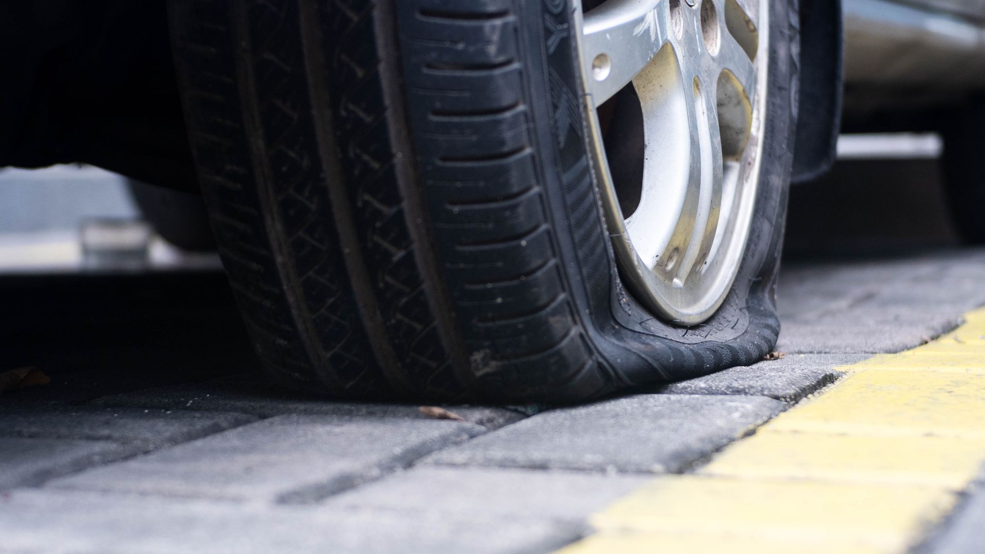 Close-up of a car tire resting on a curb beside a yellow painted line.