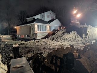 Maison située de nuit à côté d'une grande fosse de fouilles fraîchement creusée, la neige s'étant accumulée autour du site.