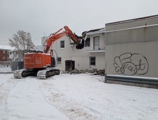 Une pelleteuse orange démolit un bâtiment blanc sur un chantier enneigé