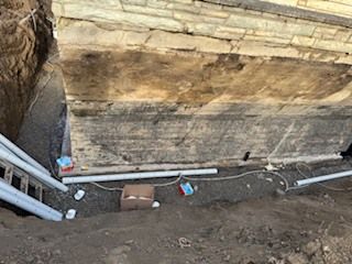 Chantier de fouilles avec mur de soutènement en béton, canalisations apparentes et sol en terre près d'une tranchée