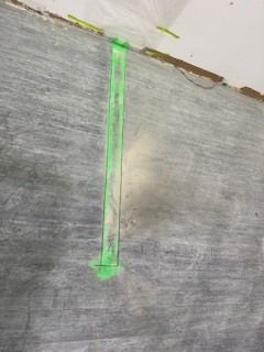 Marque fluorescente verte sur une surface en béton gris, avec une ligne verticale et une petite flèche en bas.