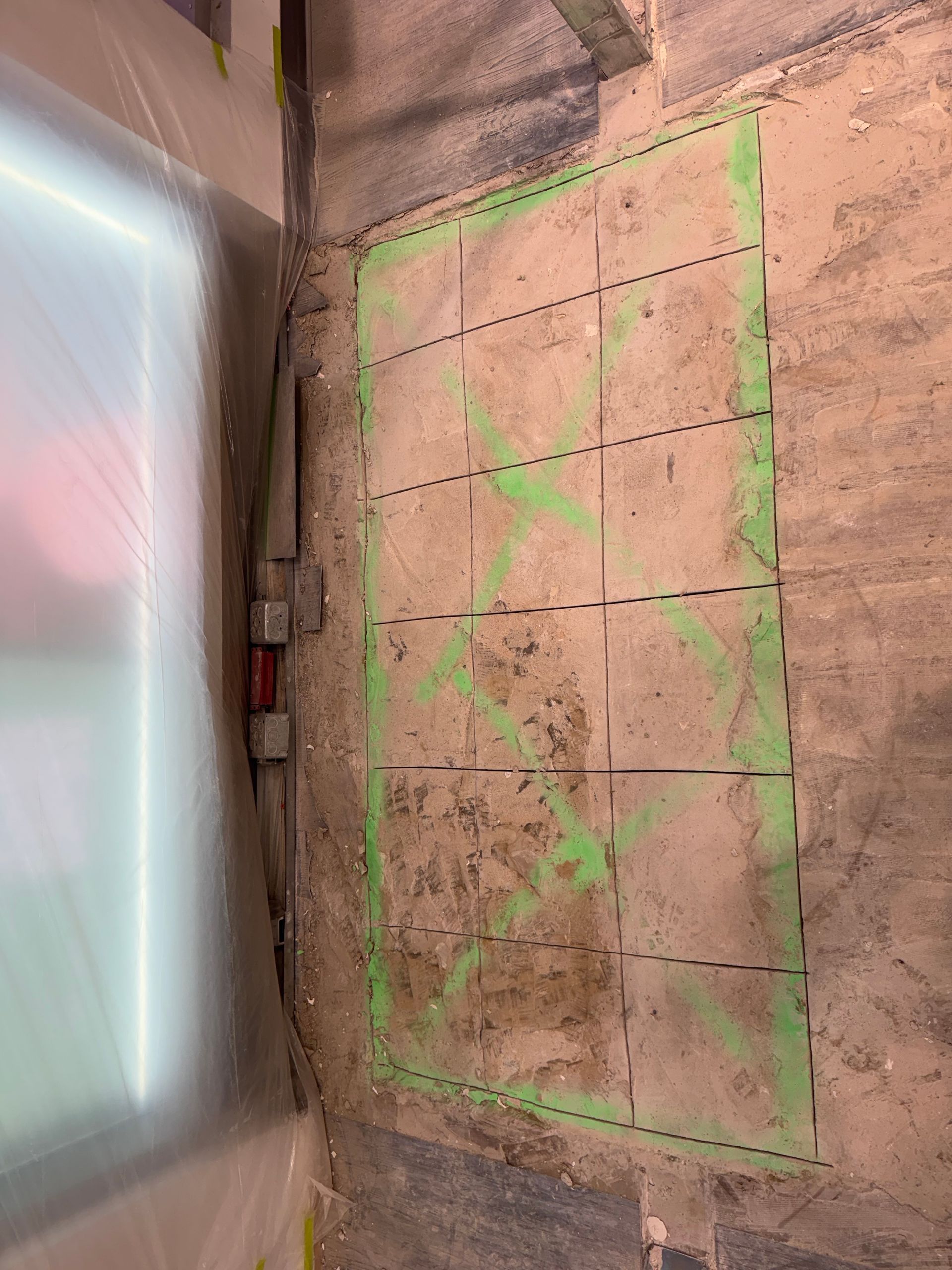 Mur de douche carrelé avec du ruban adhésif vert délimitant une zone de réparation à côté d'un panneau en verre dépoli
