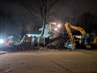 Deux excavatrices creusent de nuit un important tas de terre sur une route, sous les projecteurs de chantier.