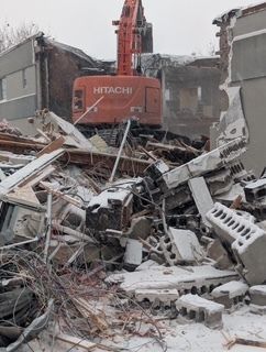 Une pelle mécanique Hitachi rouge au milieu des gravats et des débris tordus sur un site de démolition