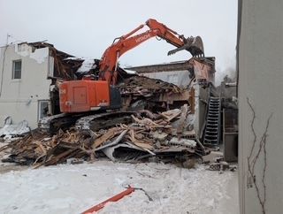 Une pelleteuse orange démolit un bâtiment effondré au milieu des décombres et de la neige.