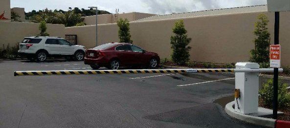 A parking lot with a barrier arm. A white SUV and red car are in the background.