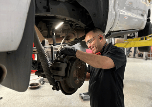Mechanic working on a car’s front wheel assembly in a garage, wearing gloves and focused on the repair