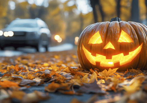 Glowing carved jack-o'-lantern on fallen leaves with a blurred car in the background