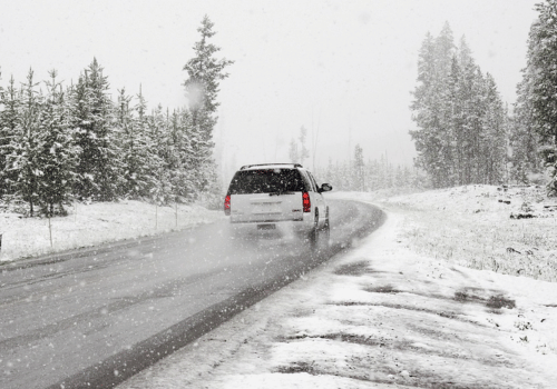 SUV driving on a snowy road through a forest during heavy snowfall