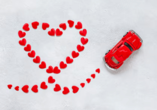Red toy car beside a heart shape made of red petals on a white background