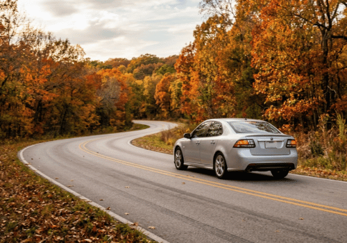 Silver sedan driving along a winding road surrounded by colorful fall foliage