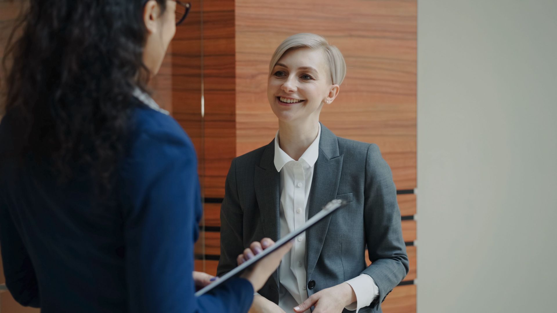 Two professionals in a meeting, one smiling while holding a tablet in an office setting
