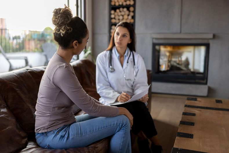 Woman talking with a doctor in a living room by a fireplace.