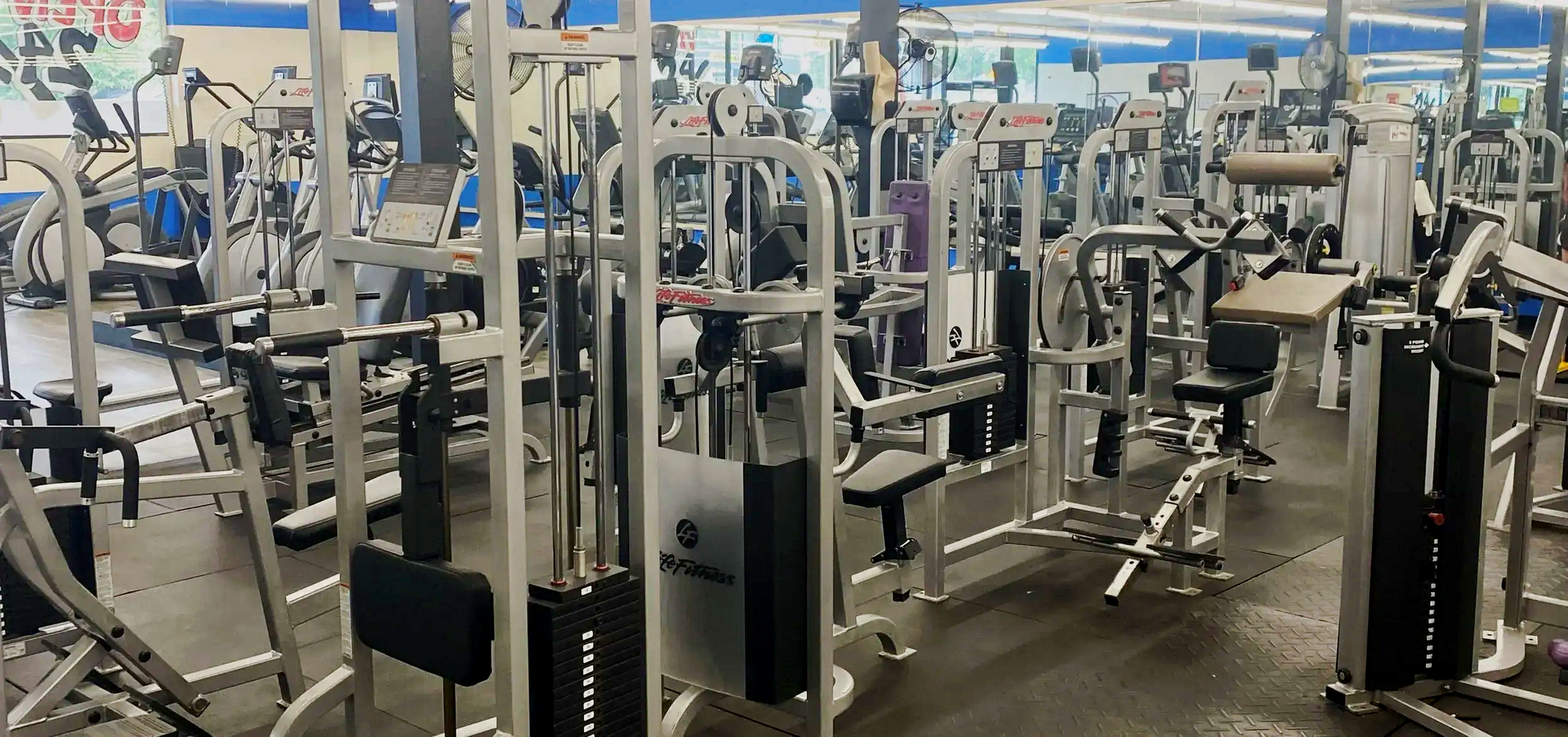 Gym interior with various weight machines, dimly lit.