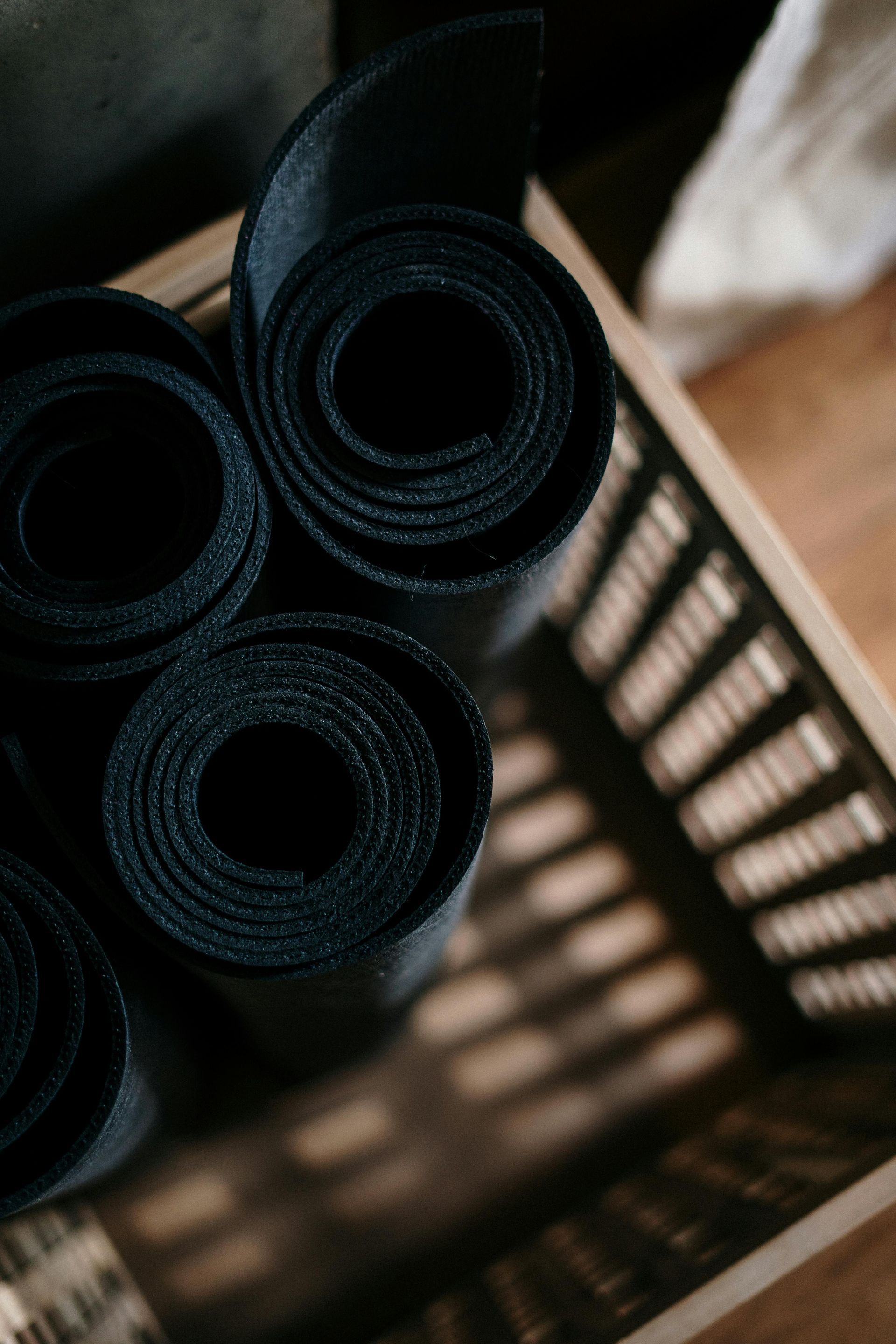 Rolled black mats in a wicker basket, with sunlight creating shadows on a brown surface.