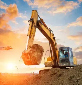 Excavator lifts a large dirt clump at sunset on a construction site.