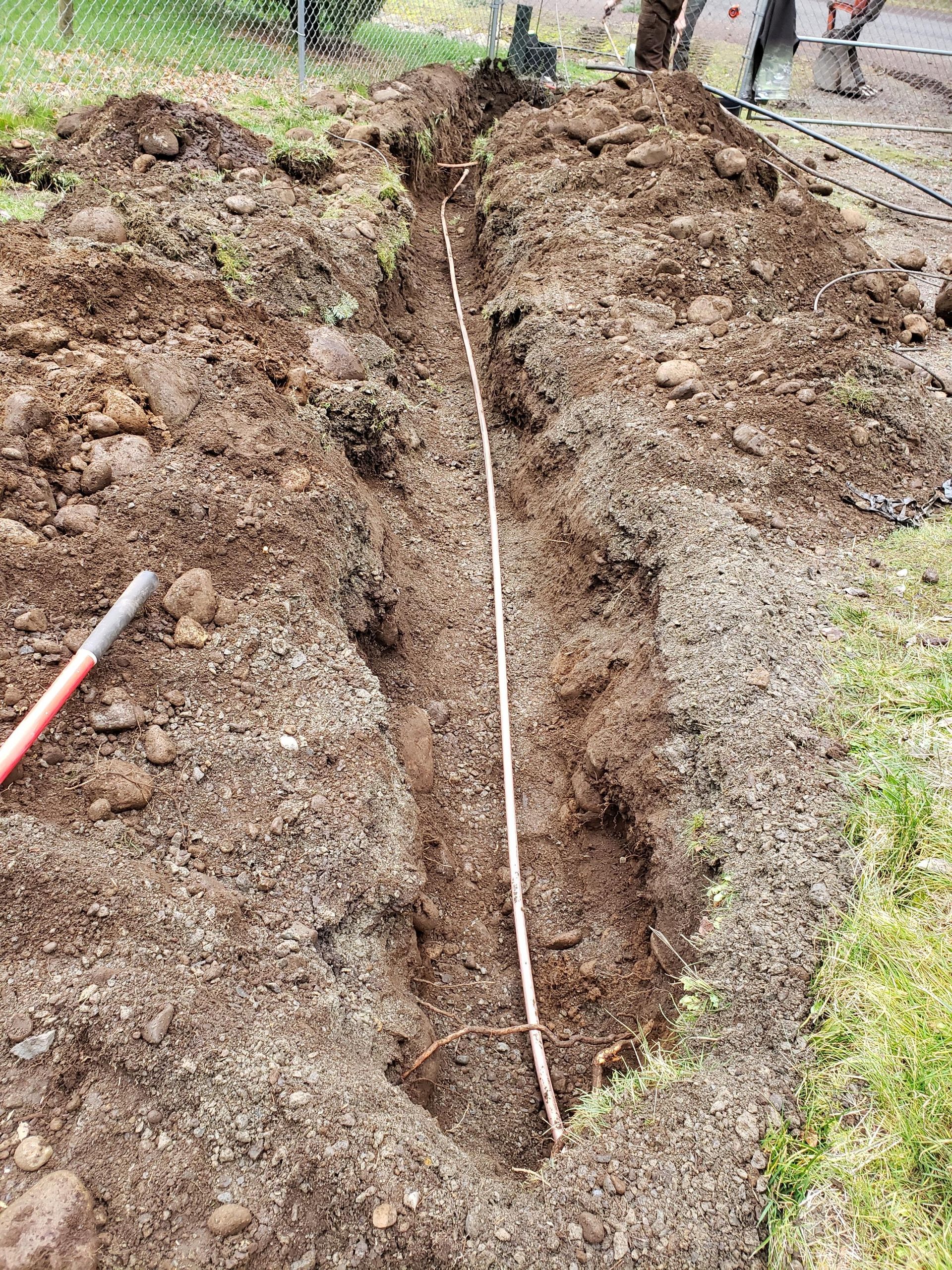 Open trench with blue PVC pipes and white conduit at a construction site.
