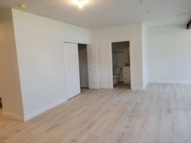 Empty white room with light wood flooring and a small kitchen alcove