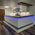 Modern home bar with blue LED lighting, white paneling, dark countertop, and wall-mounted TV