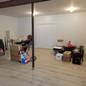 Cluttered unfinished room with boxes, furniture, and a central support pole on a wood floor