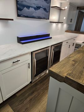 Modern kitchen with white cabinets, wood island, and black under-counter beverage coolers with blue lighting