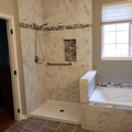 Modern marble-tiled bathroom with a walk-in shower, bathtub, and window.