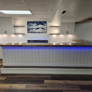 Empty modern reception desk with blue underlighting, white walls, and a cloud painting above.