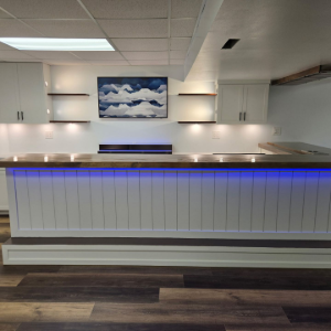 Empty modern reception desk with blue underlighting, white walls, and a cloud painting above.