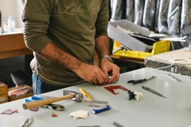 Person assembling tools on a worktable in a workshop, with pliers, screwdrivers, and tape scattered around.