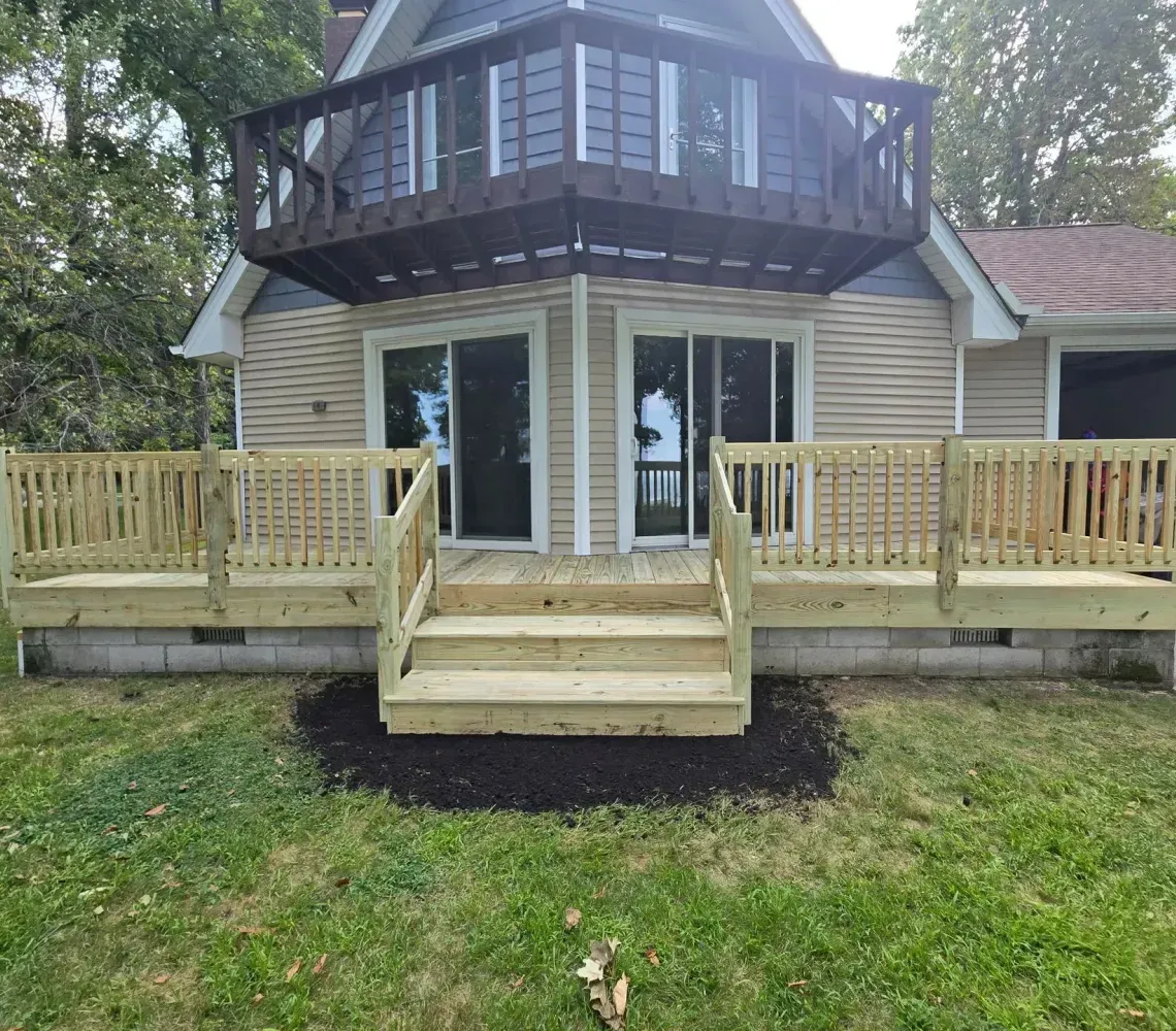 Small house with a raised octagonal sunroom, front steps, and two wooden deck platforms in a grassy yard.