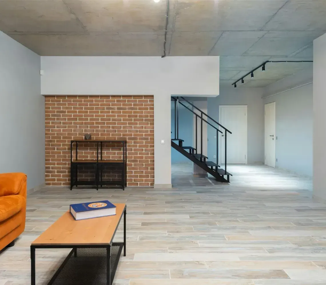 Modern living room with orange sofa, brick fireplace, and black staircase.