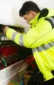 Technician in a neon yellow jacket inspecting wiring inside an open electrical panel